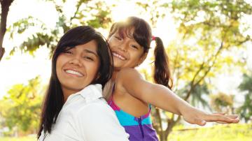 Hispanic mother carrying her daughter on her back